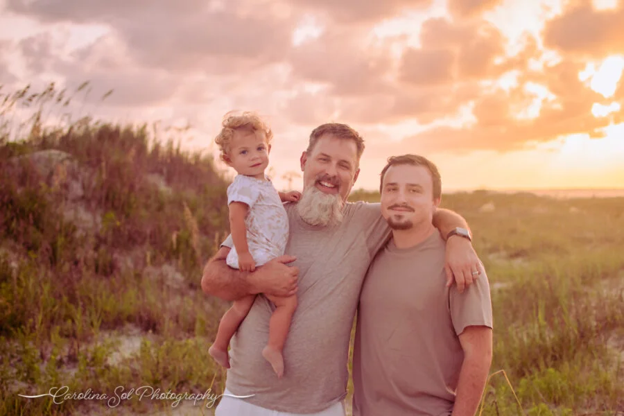 Father and two sons standing in front of colorful sunset during summer family photography.