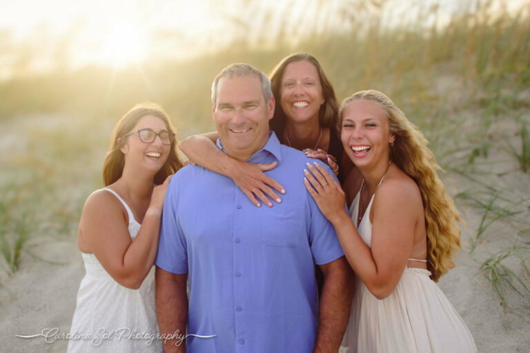 Family laughing together while sharing a group hug on holden beach, nc during the golden hour sunset.