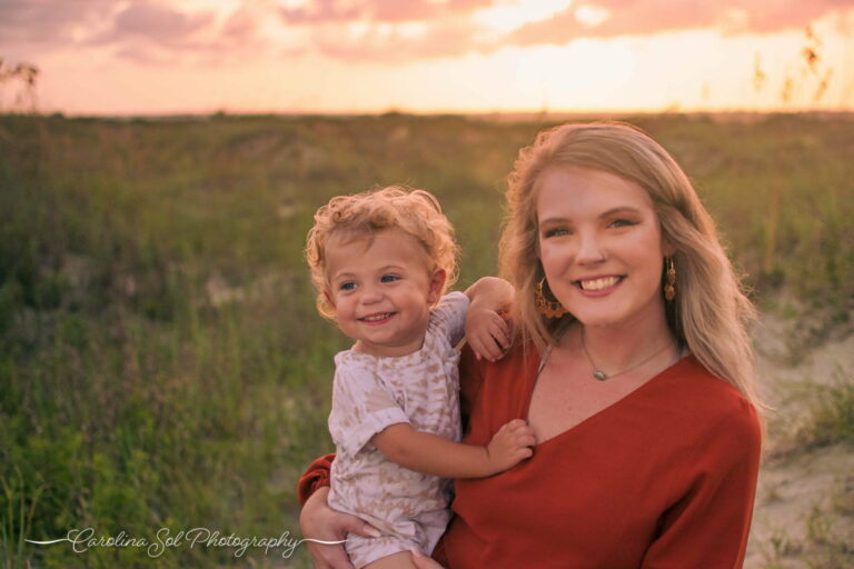 Siblings smiling near the beachgrass on sunset beach during their family portrait photography session.